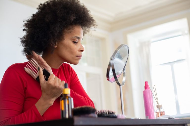 Femme aux cheveux crépus réalisant sa routine capillaire devant un miroir